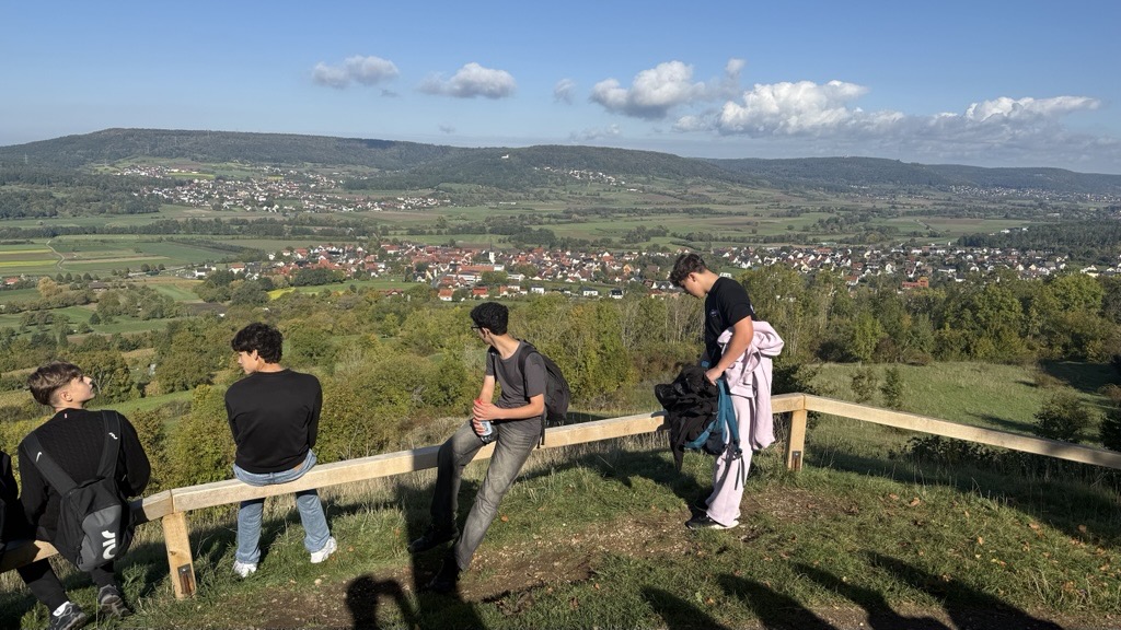 Schüler sitzen auf einer Einzäunung aus Holz und genießen den Ausblick